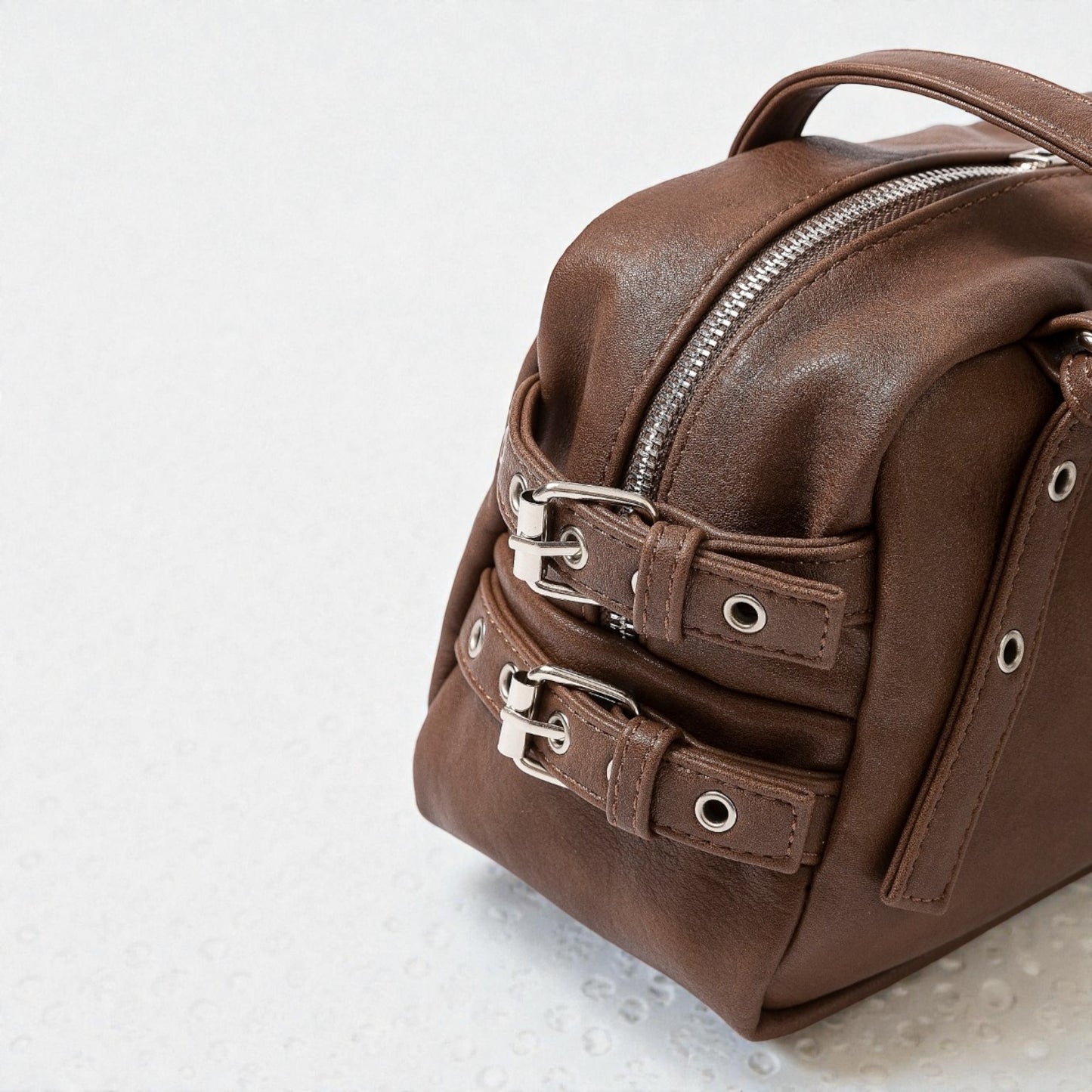 Brown leather bag with silver zippers on a light gray background