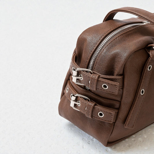 Brown leather bag with silver zippers on a light gray background