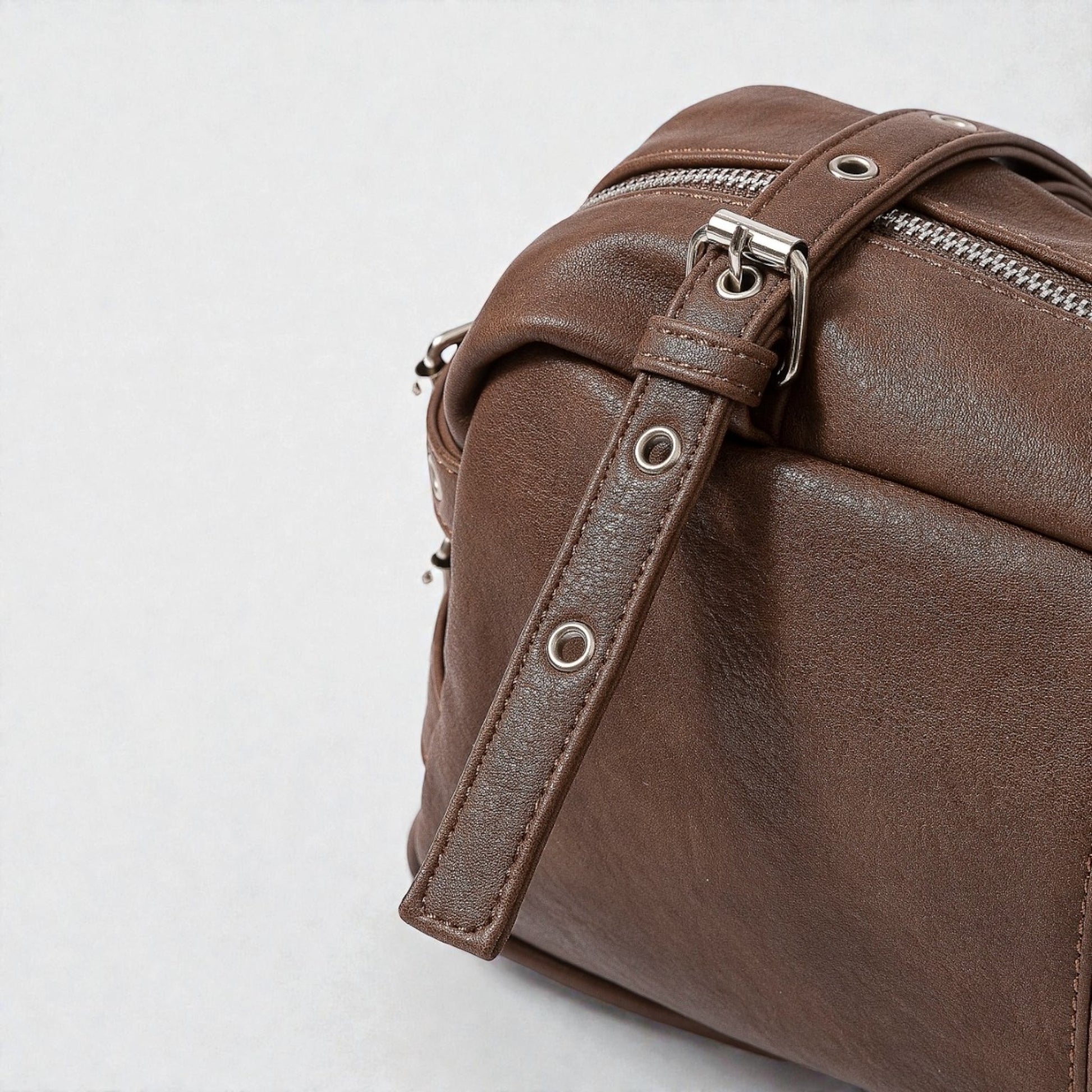 Brown leather bag with a strap on a light gray background