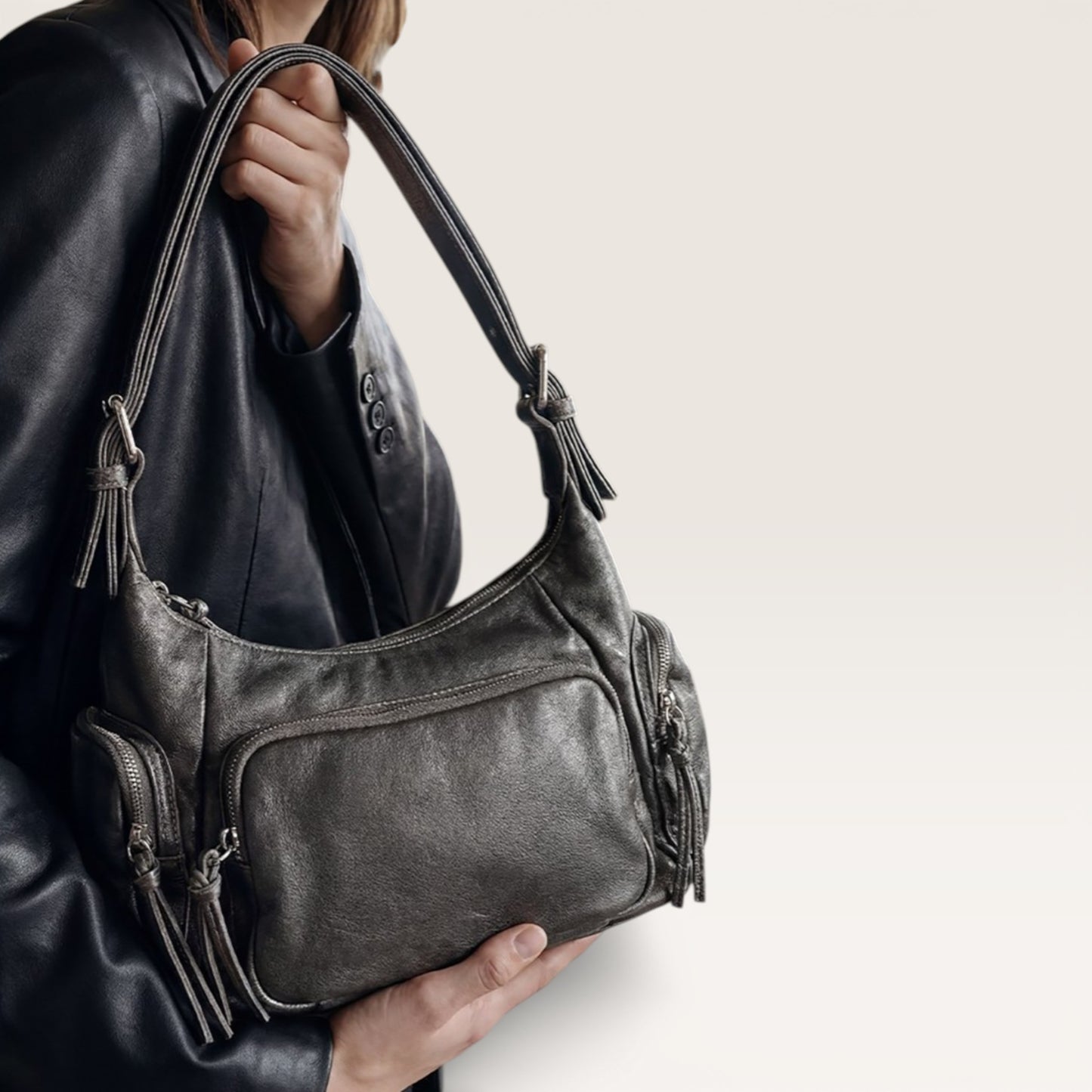 Person holding a dark gray leather handbag with tassels on a light background