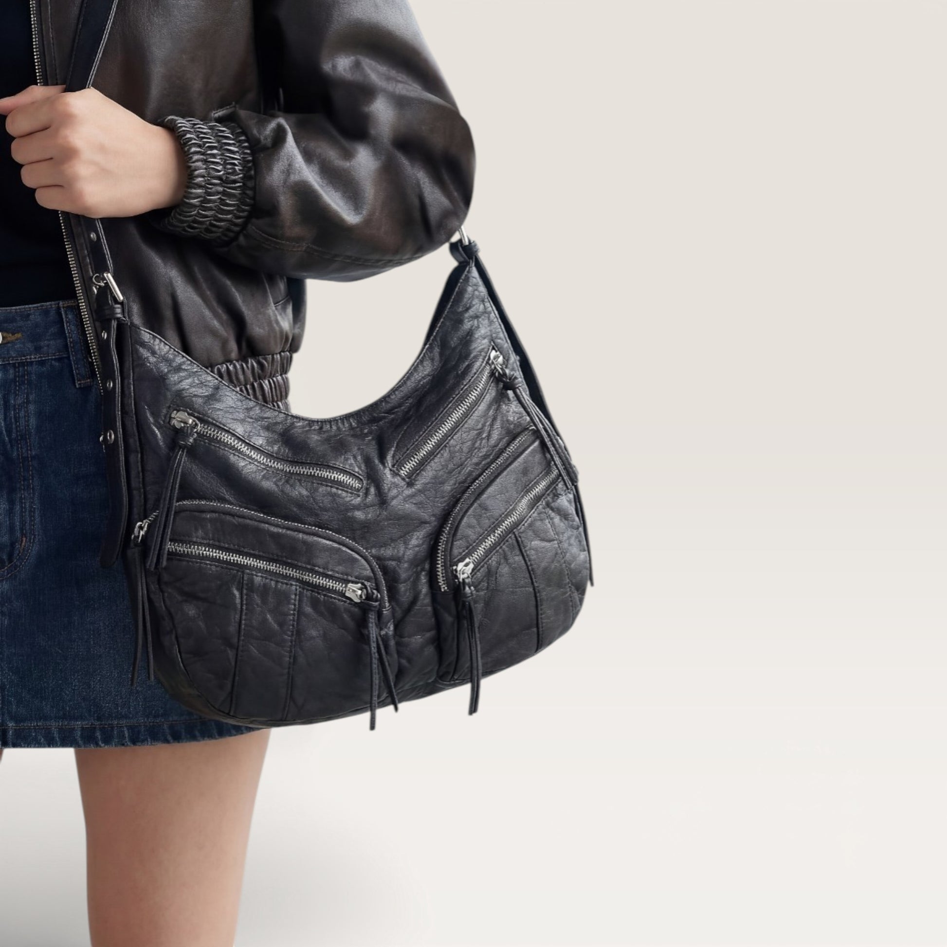 Person holding a black leather handbag with a neutral background