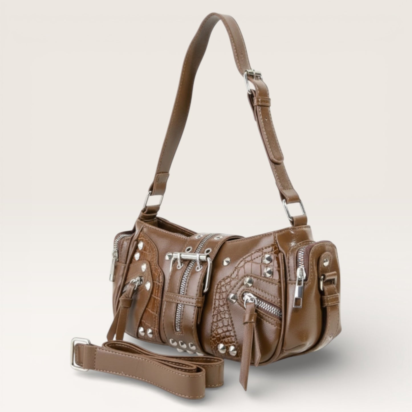 Brown handbag with silver studs and zippers on a light gray background