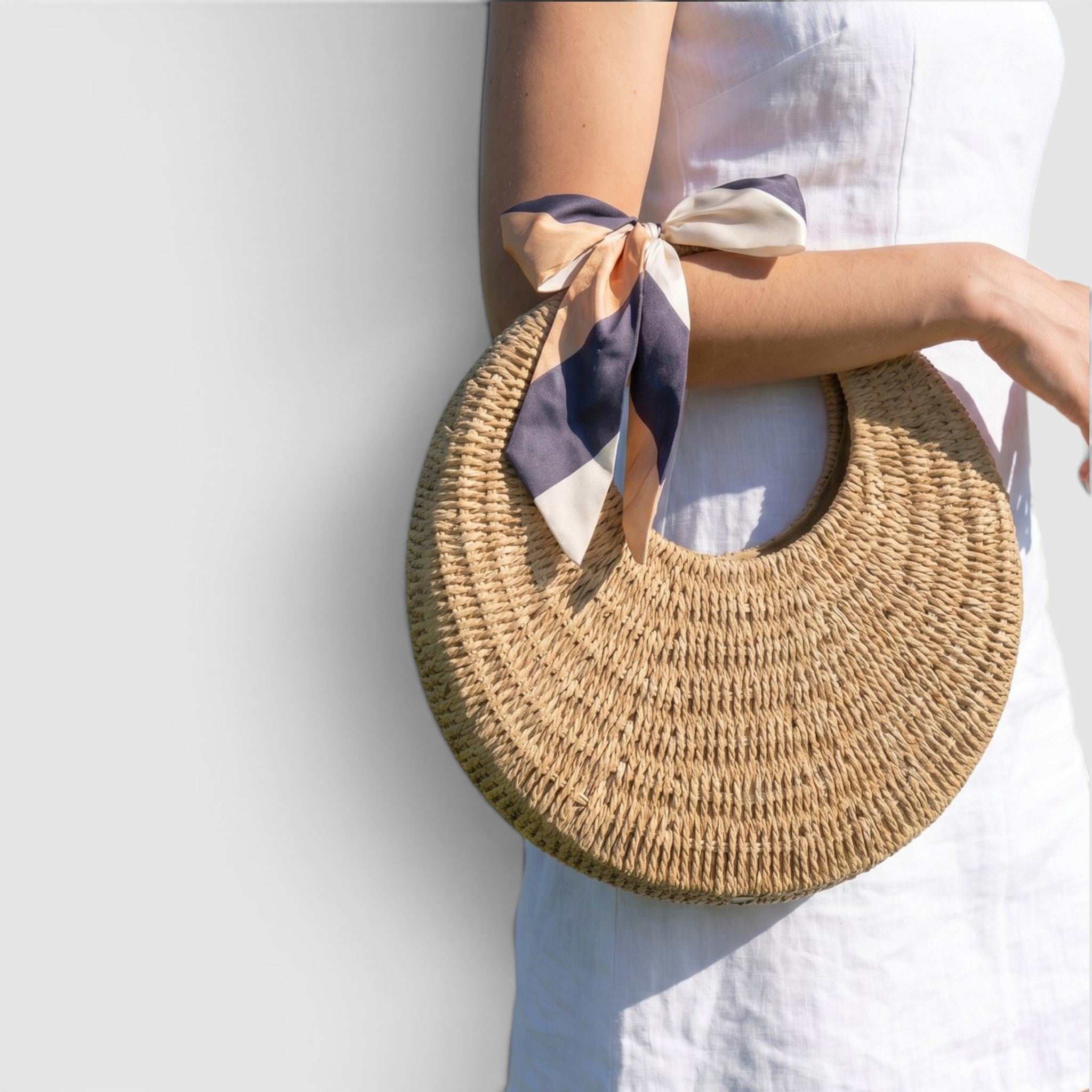 Round woven bag with a scarf over the elbow against a light background