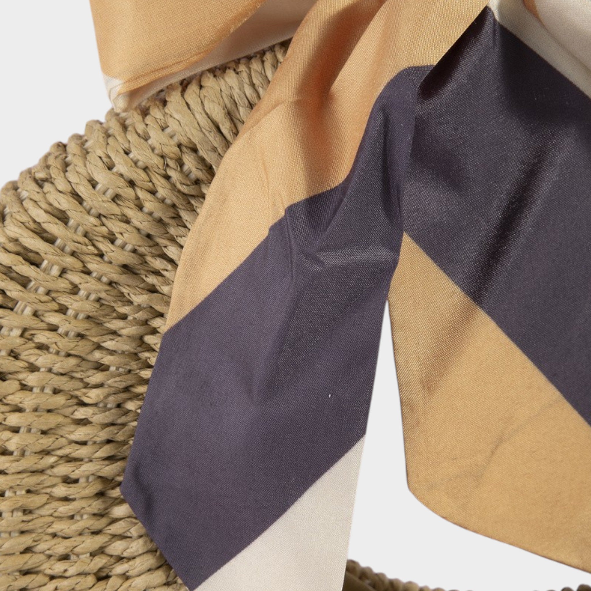 Close-up of a fabric with purple, beige, and white stripes draped over a woven surface.