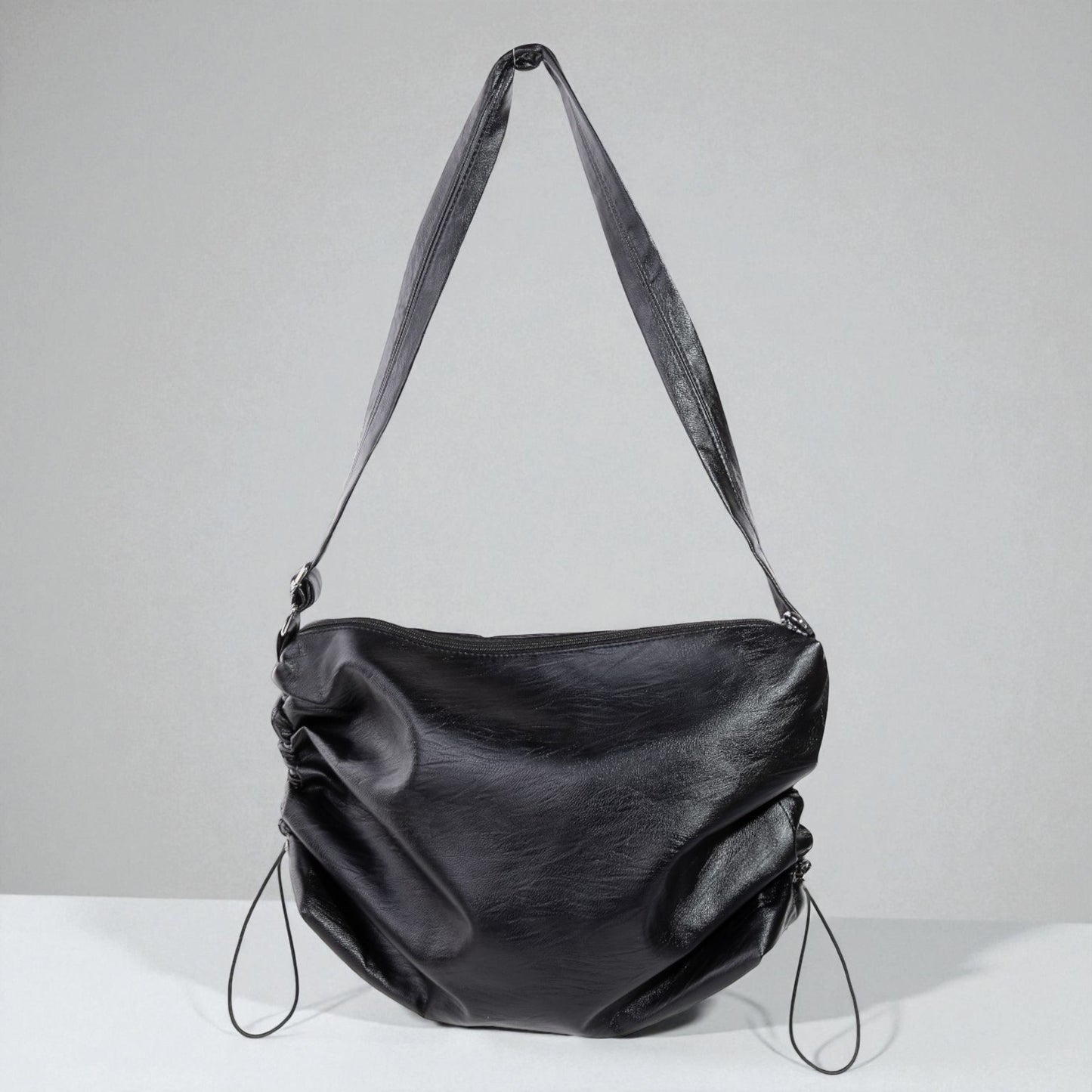 Black leather handbag with a strap on a light gray background