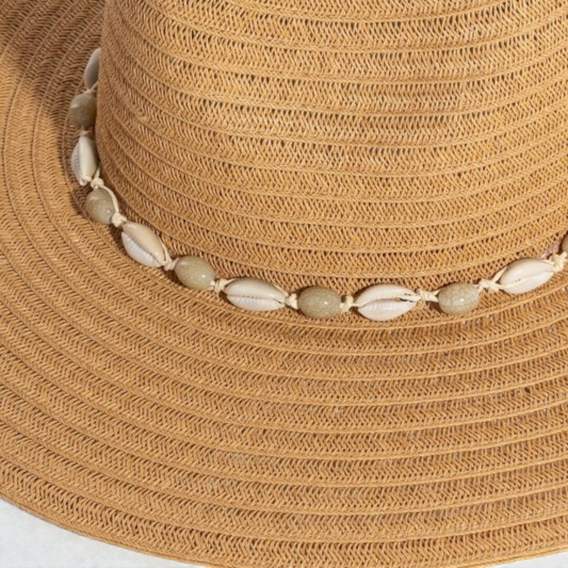 Beige straw hat with a decorative shell band on a white background