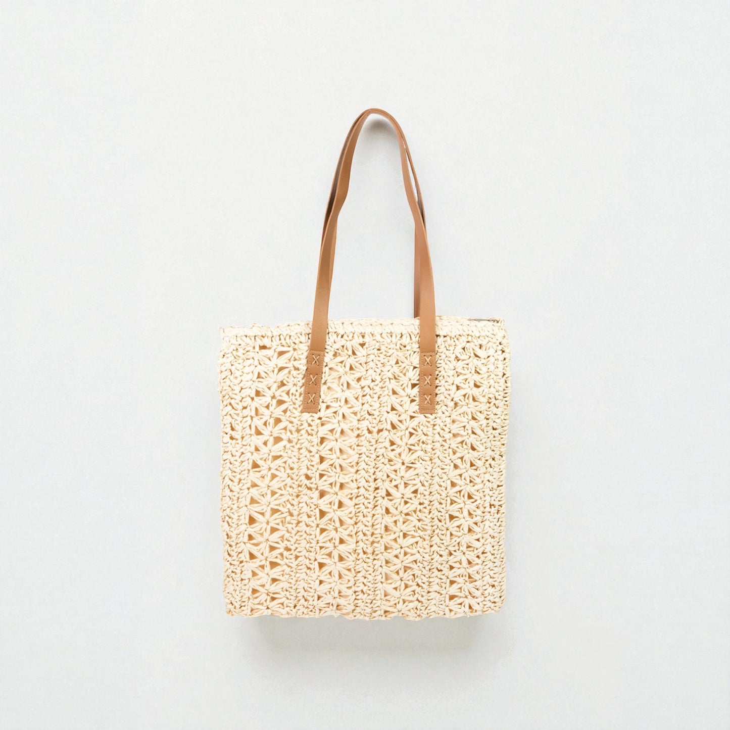 Woven tote bag with brown leather straps on a light gray background