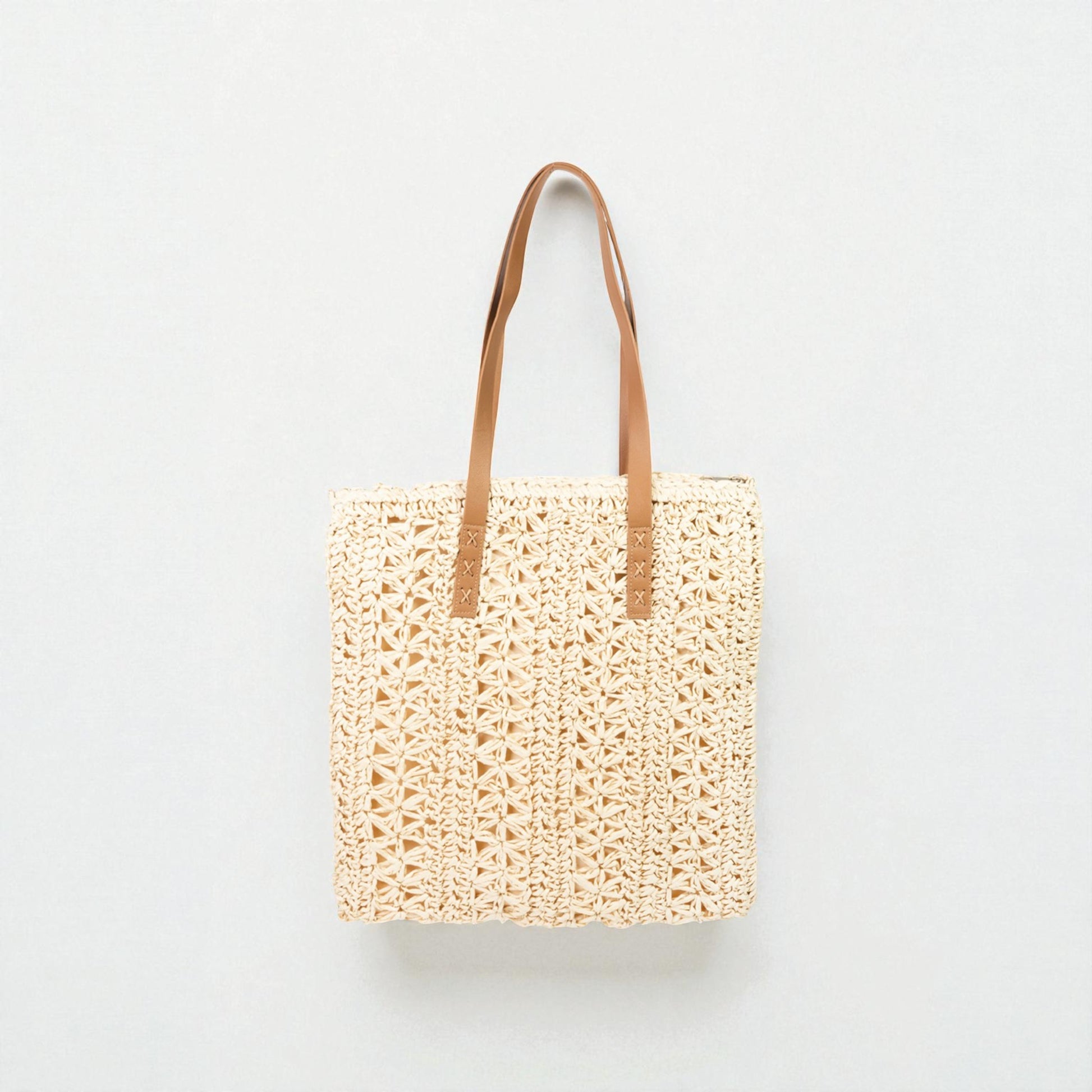 Woven tote bag with brown leather straps on a light gray background