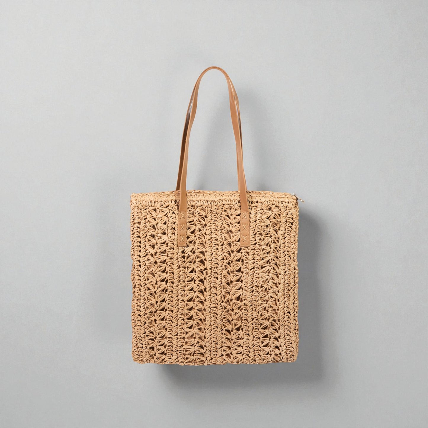Woven tote bag with leather handles on a gray background
