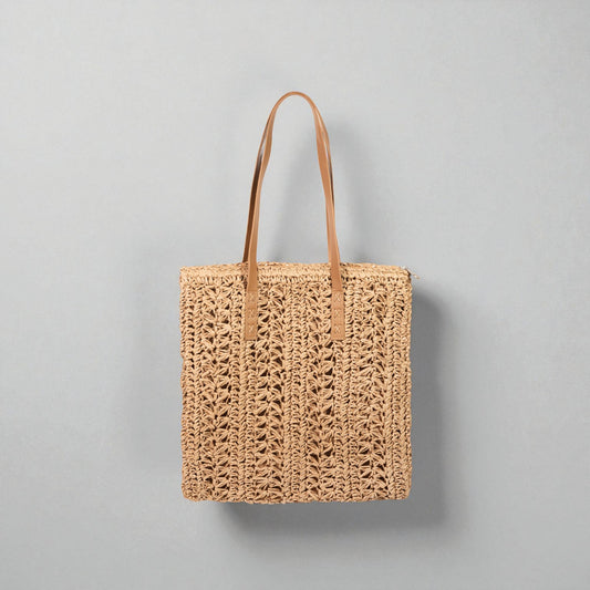 Woven tote bag with leather handles on a gray background