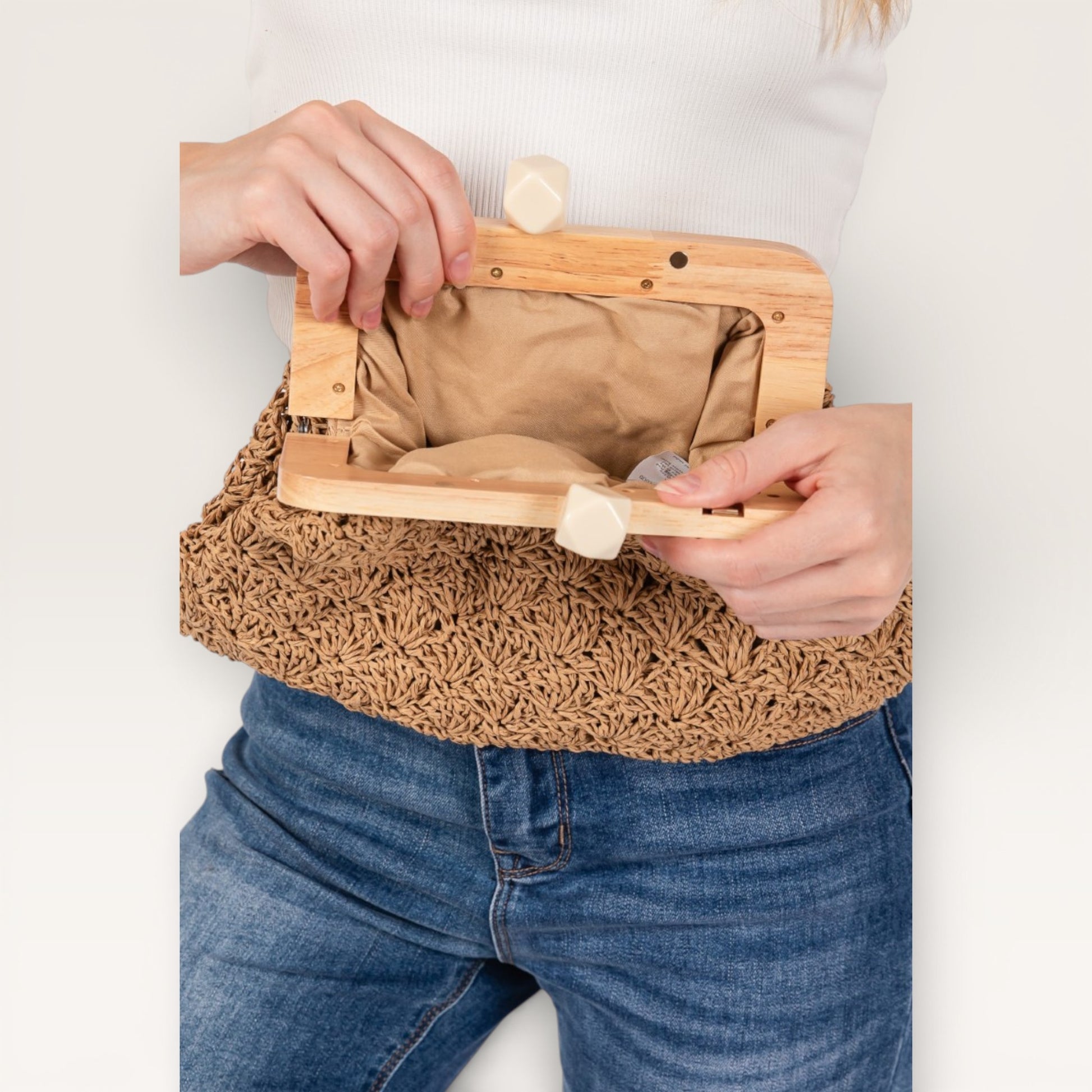 Person holding a woven handbag with wooden clasp and beige interior.