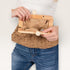 Person holding a woven handbag with wooden clasp and beige interior.