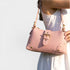 Pink handbag with gold accents held by a person against a light background
