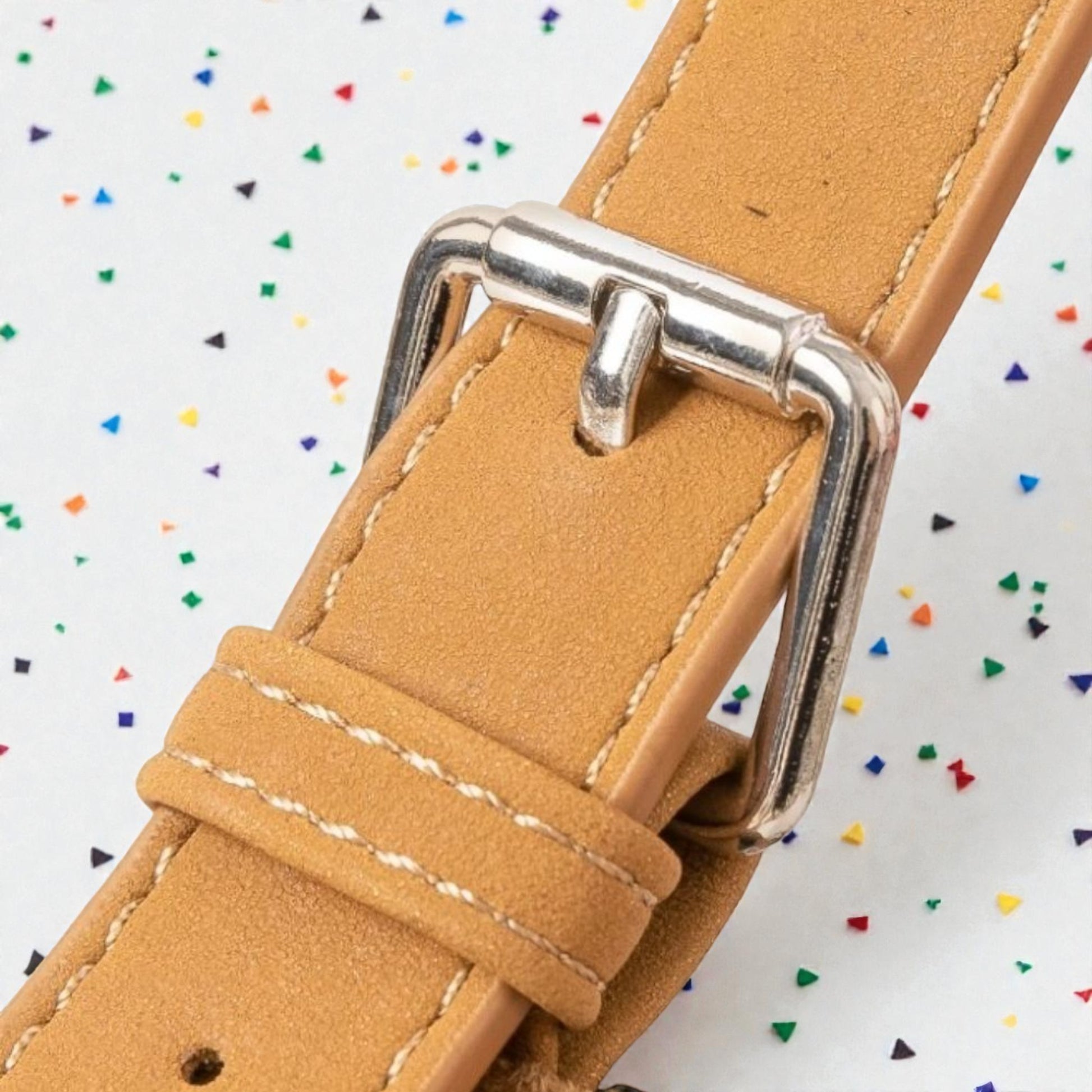 Close-up of a tan leather watch strap with a silver buckle on a colorful confetti background