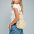Woman wearing a beige crossbody bag against a gray background