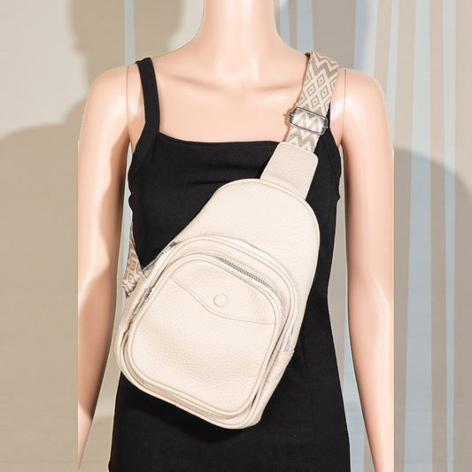 Mannequin wearing a beige crossbody bag with a patterned strap against a neutral background