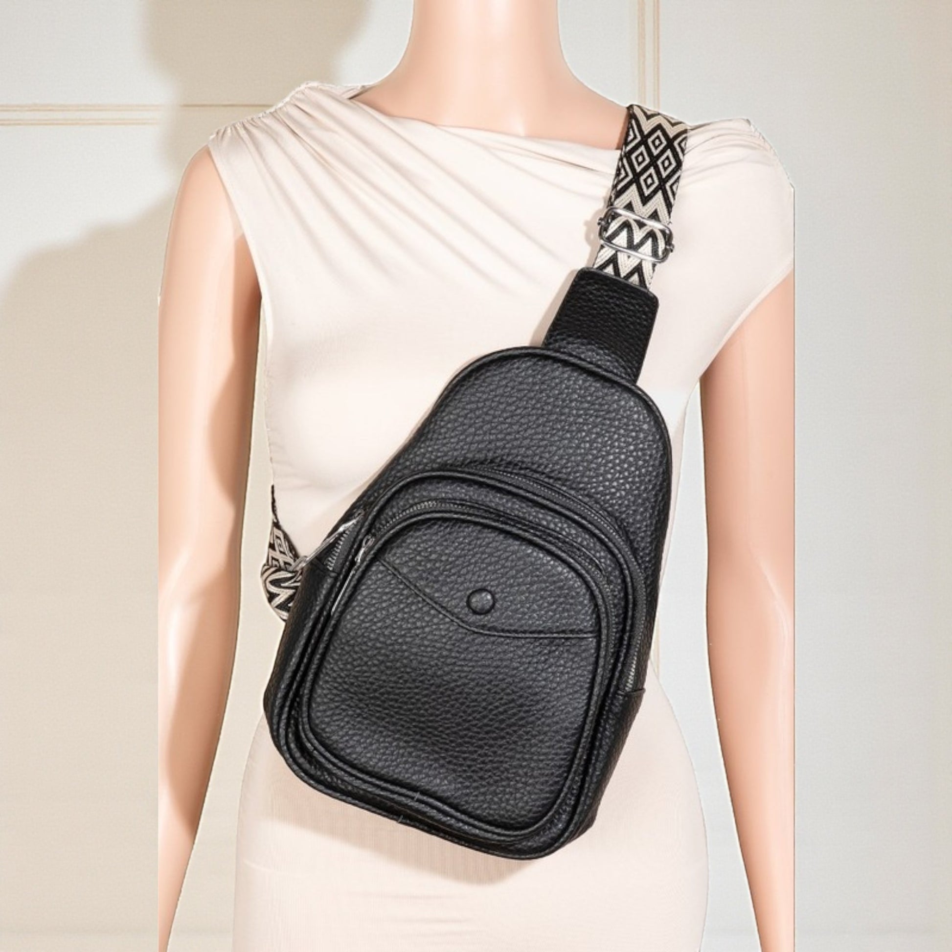 Black leather sling bag on a mannequin with a plain background