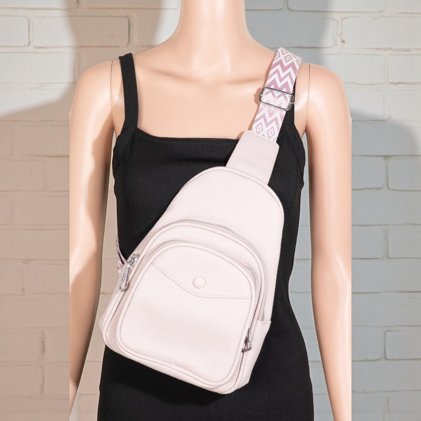 Mannequin wearing a black dress with a pink sling bag against a light brick wall.