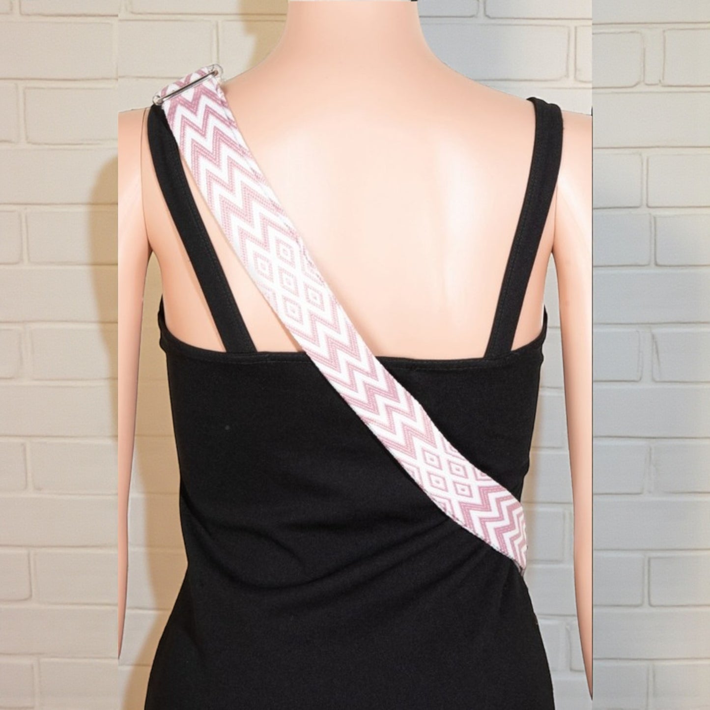 Mannequin wearing a black dress with a pink and white zigzag sash against a tiled wall.