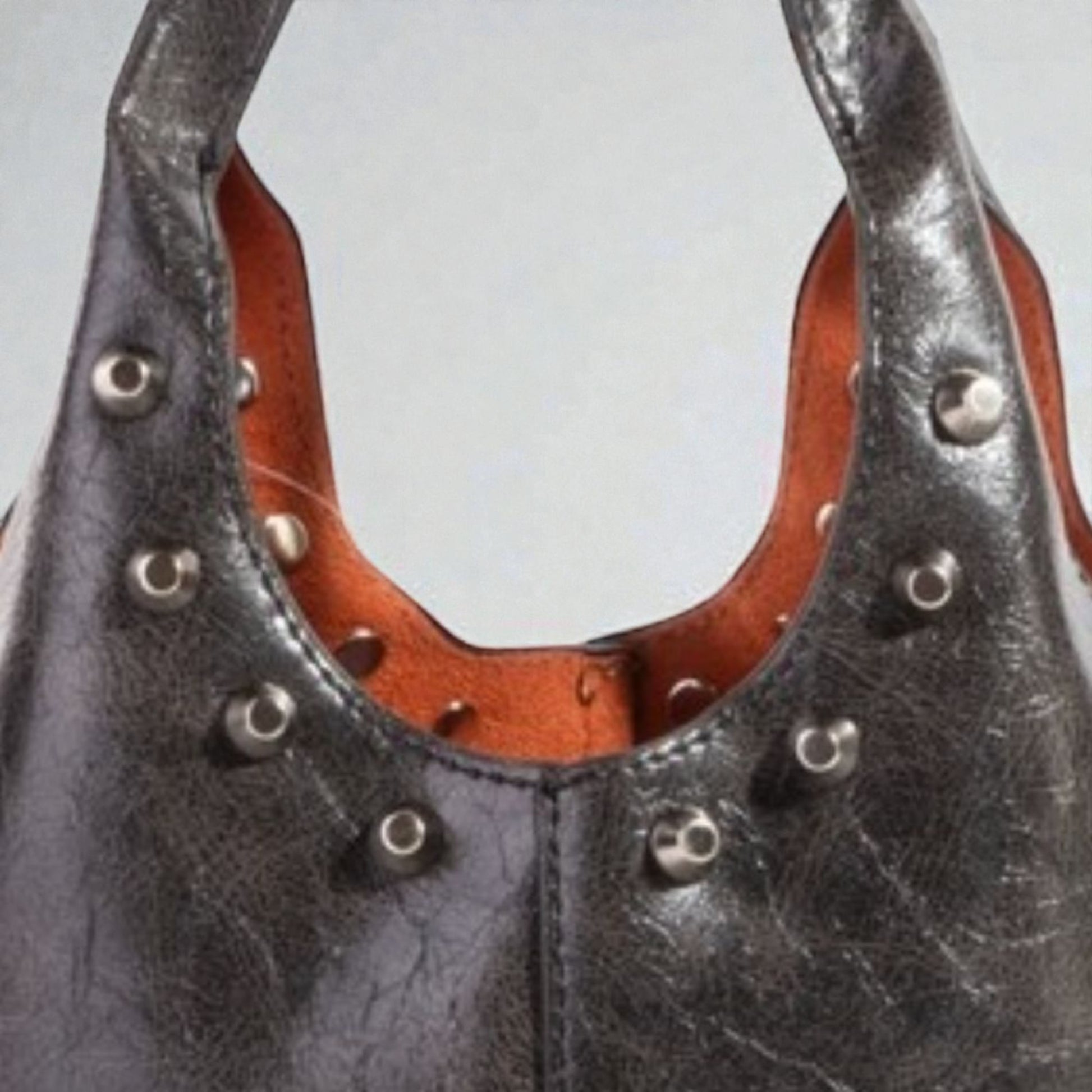Close-up of a black leather handbag with brown interior and silver studs on a light gray background