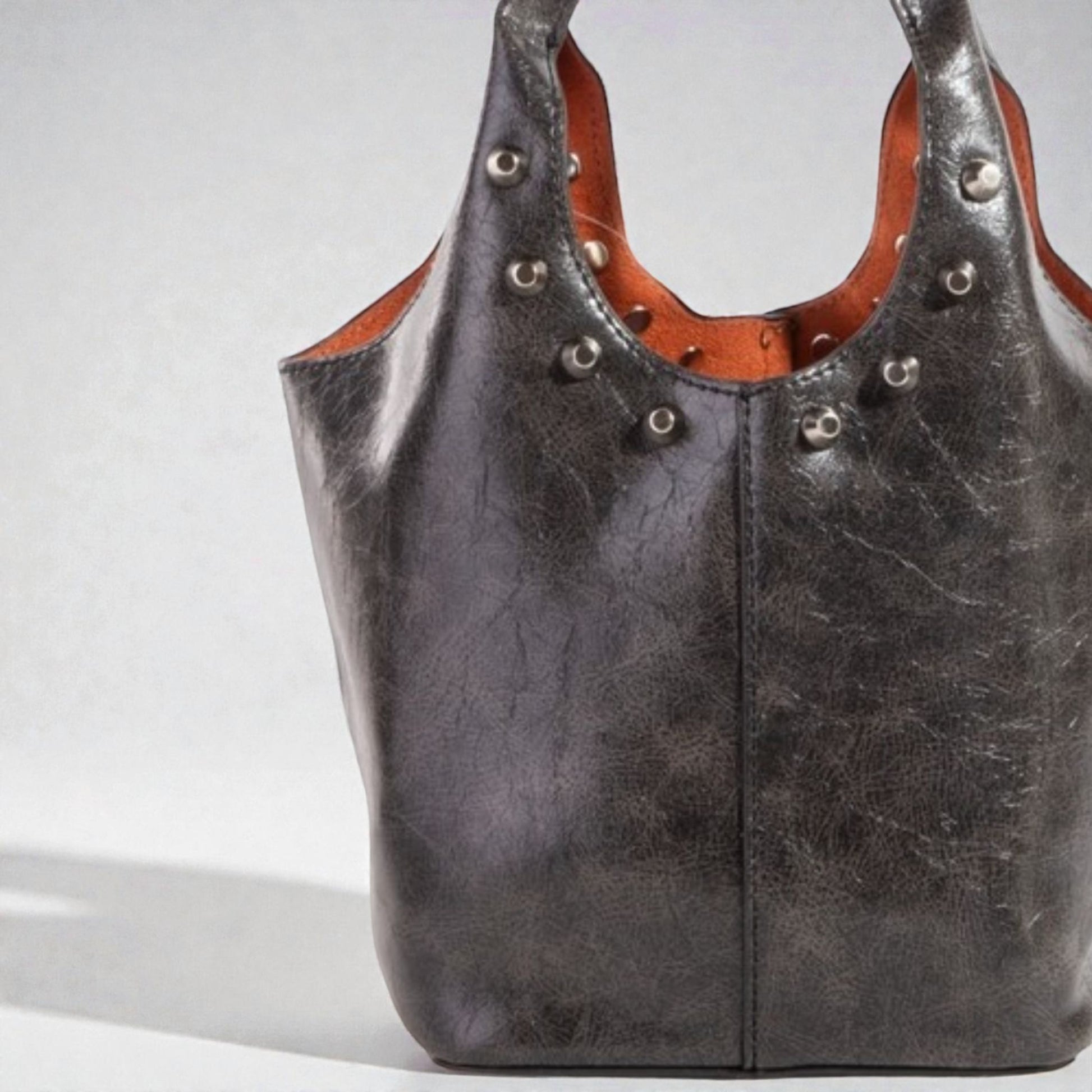 Dark brown leather handbag with studs on a light gray background
