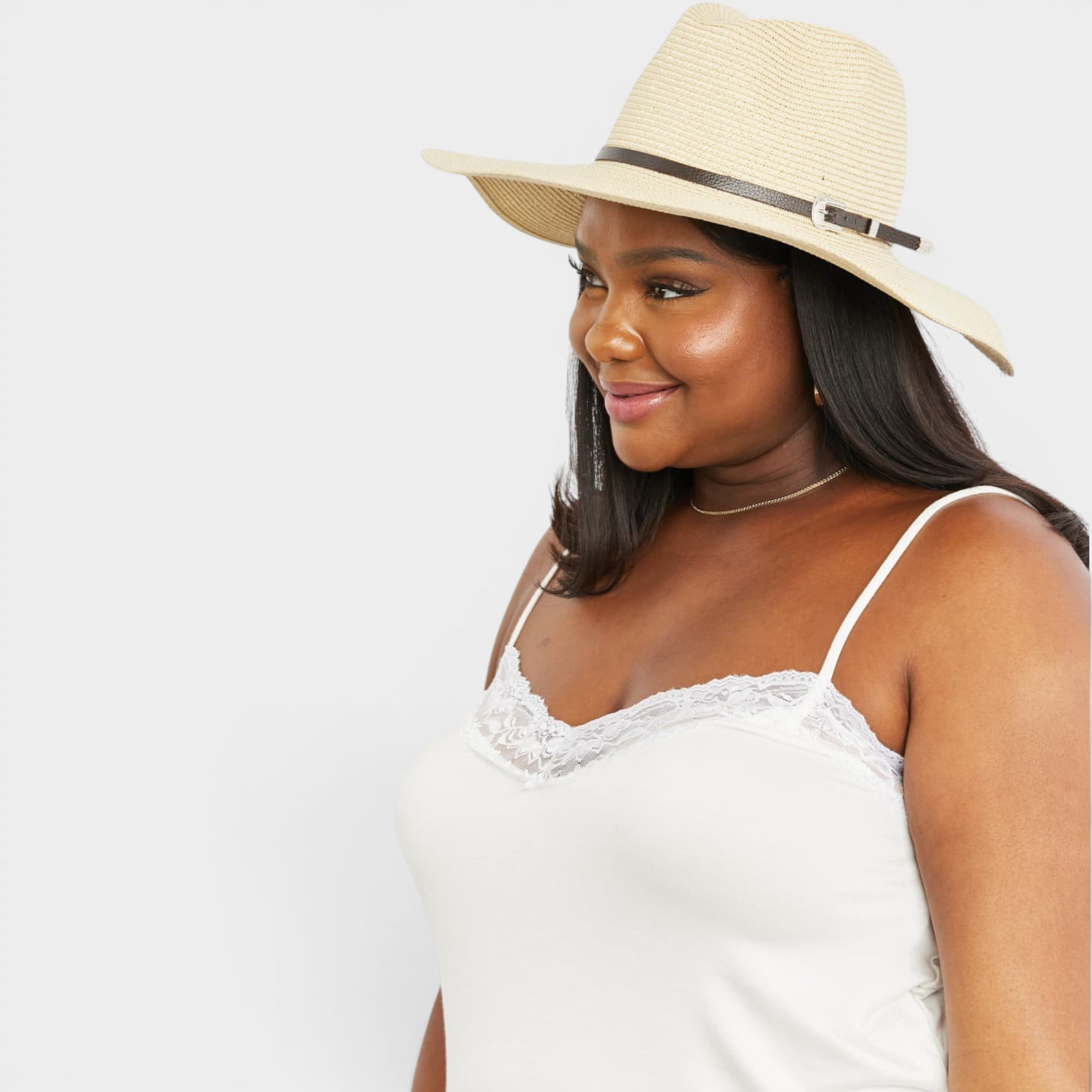 Woman wearing a white lace top and straw hat on a plain background