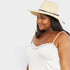 Woman wearing a white lace top and straw hat on a plain background