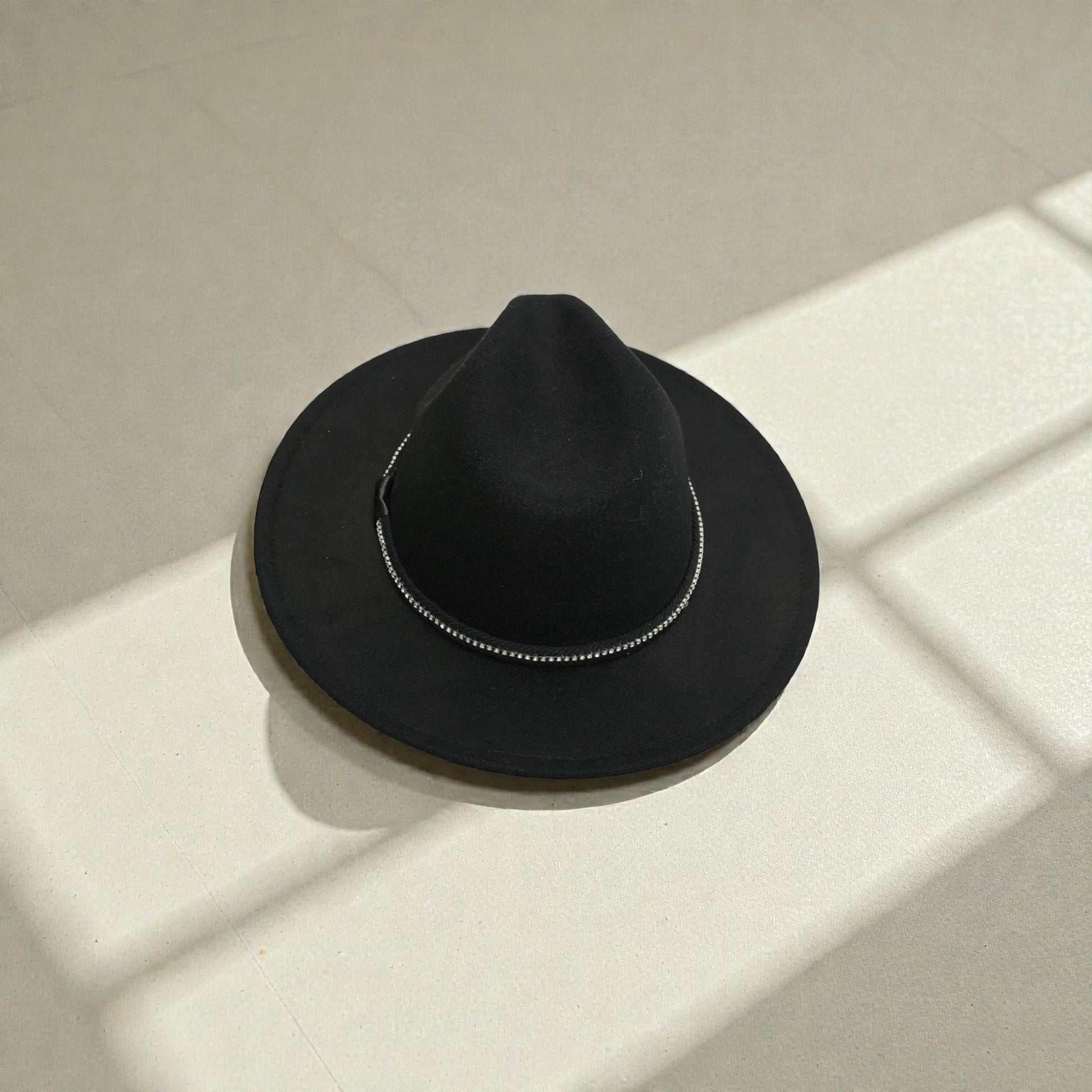 Black fedora hat on a light surface with shadows