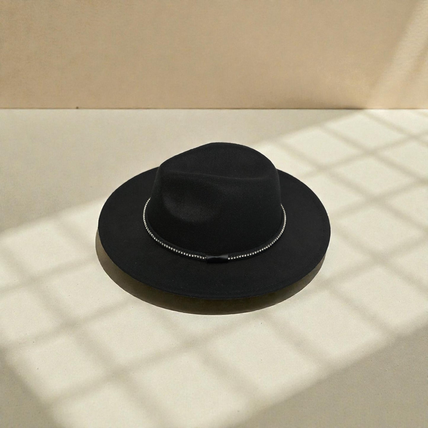 Black fedora hat on a beige surface with soft shadows