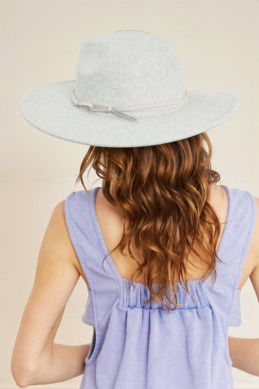 Woman wearing a light gray hat and a purple sleeveless top on a beige background