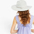 A woman shown from behind wearing a light gray felt wide-brim hat with a thin ribbon band and bow, paired with a lavender sleeveless top against a plain white background.