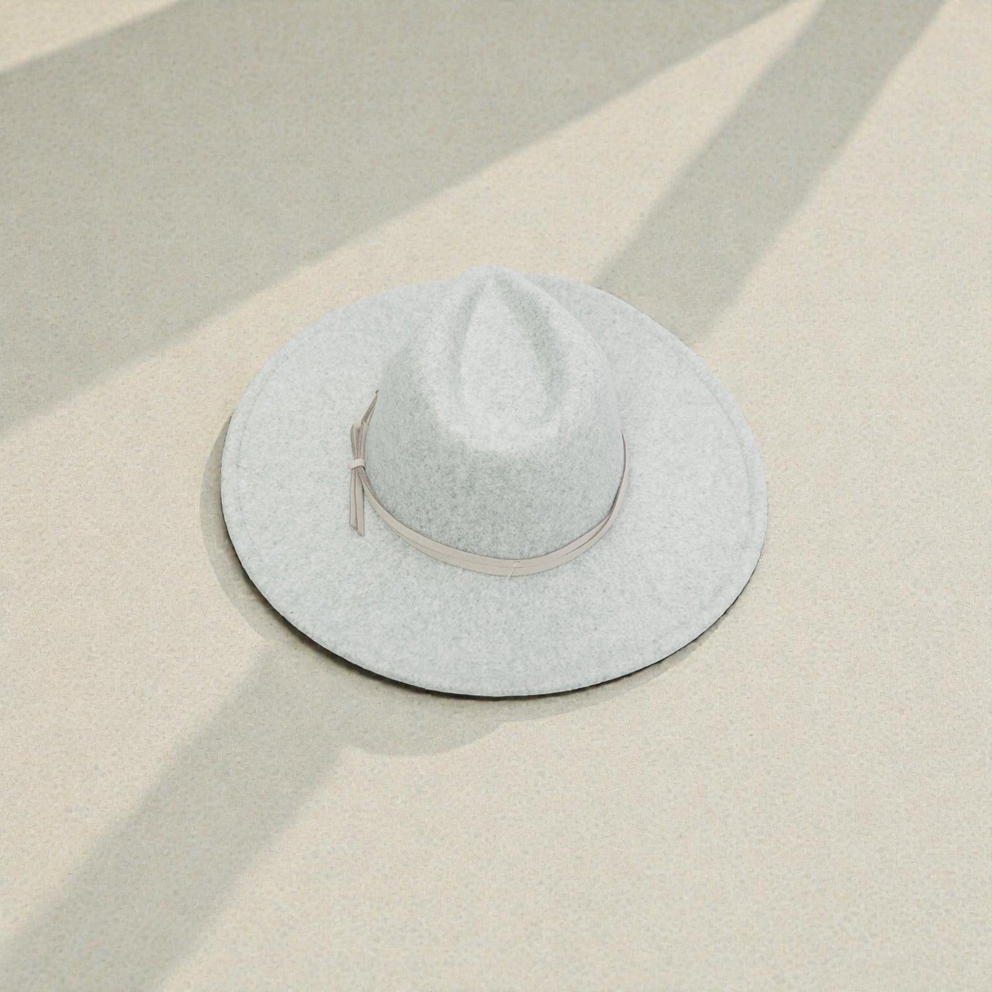 Light gray fedora hat on a beige surface with soft shadows