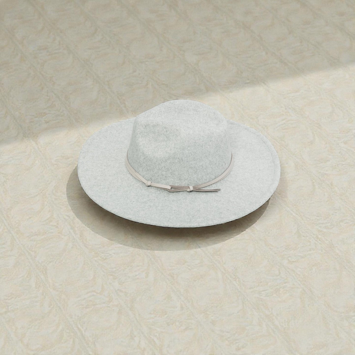 Light gray sun hat with a ribbon on a textured beige surface
