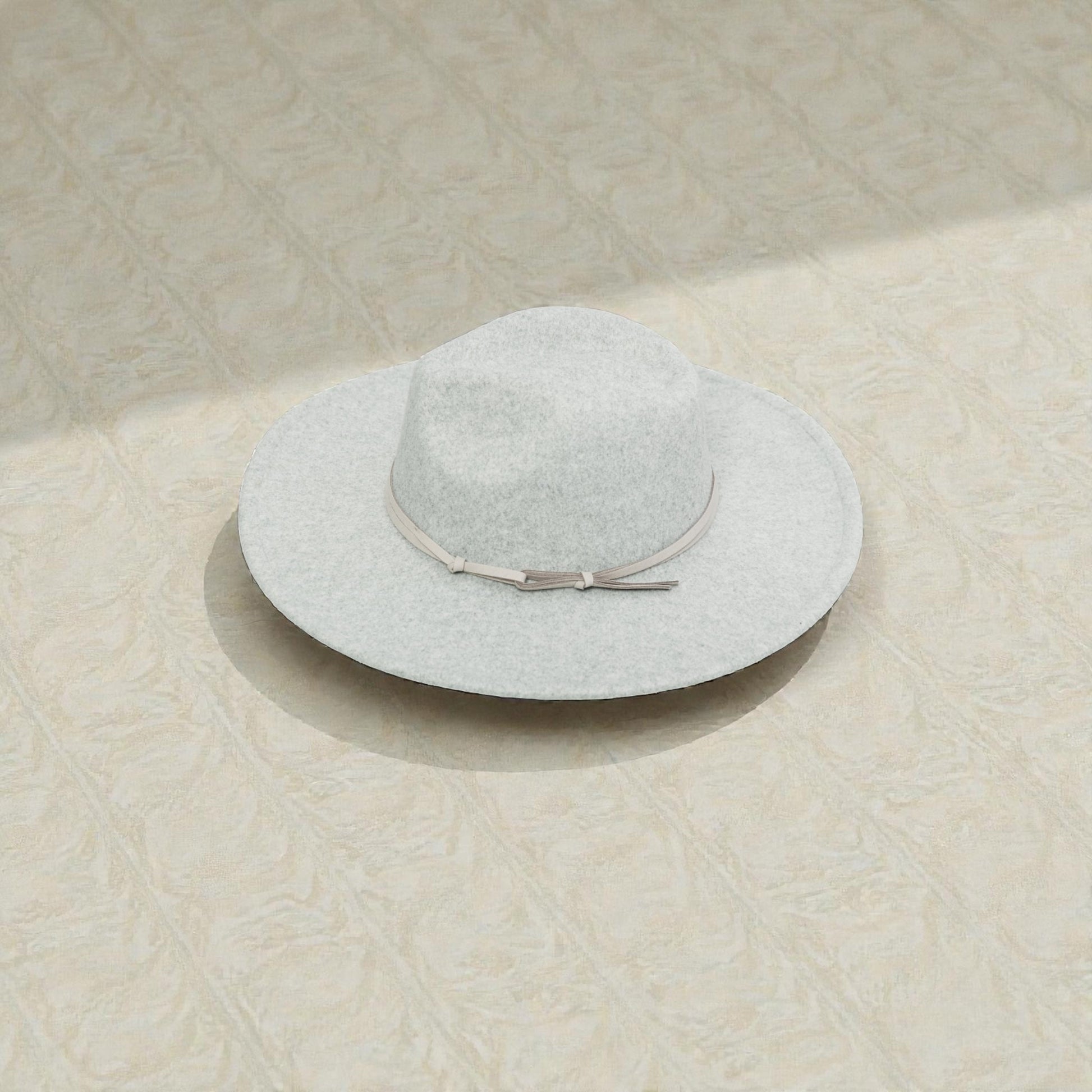 Light gray sun hat with a ribbon on a textured beige surface