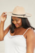Woman wearing a beige hat with a black band against a plain background