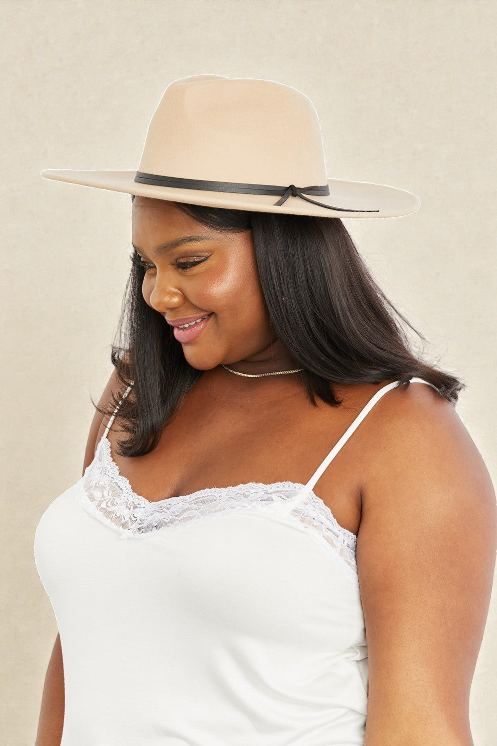 Woman wearing a beige hat and white lace top against a beige background