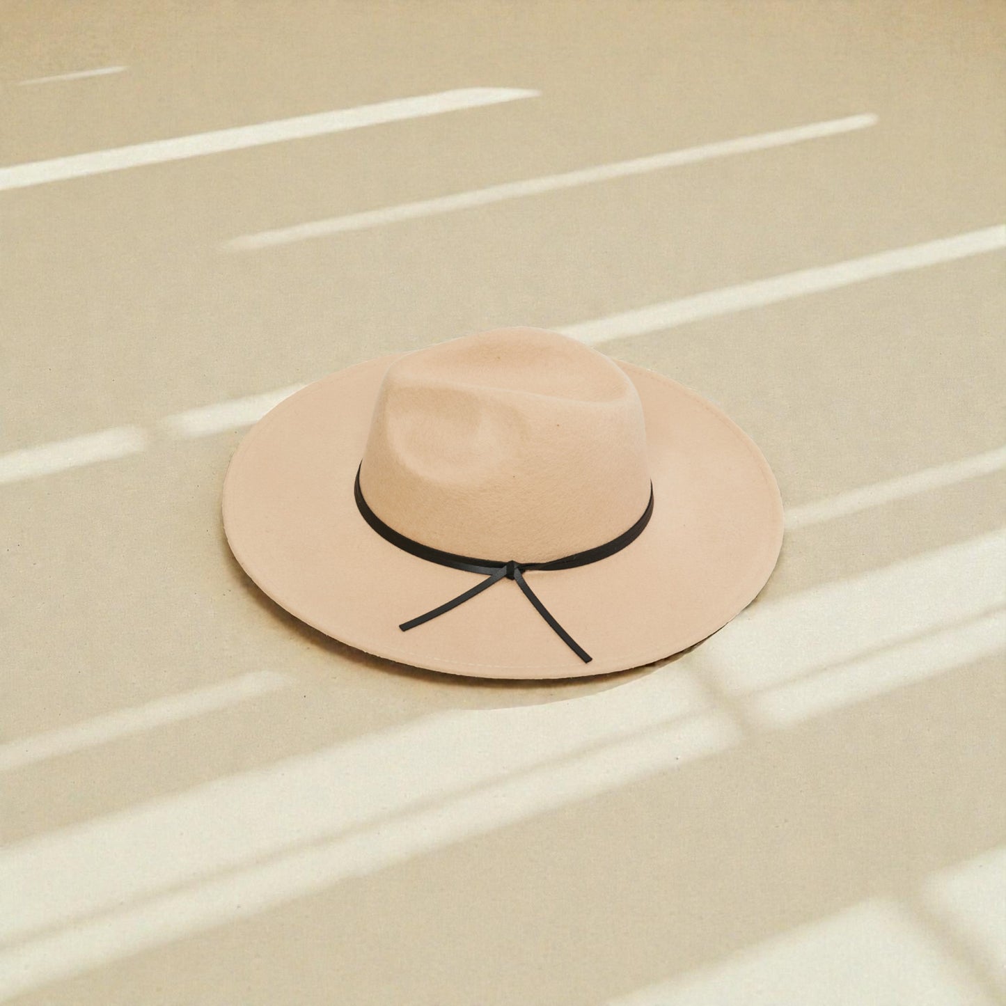 Beige hat with black band on a beige surface with white lines