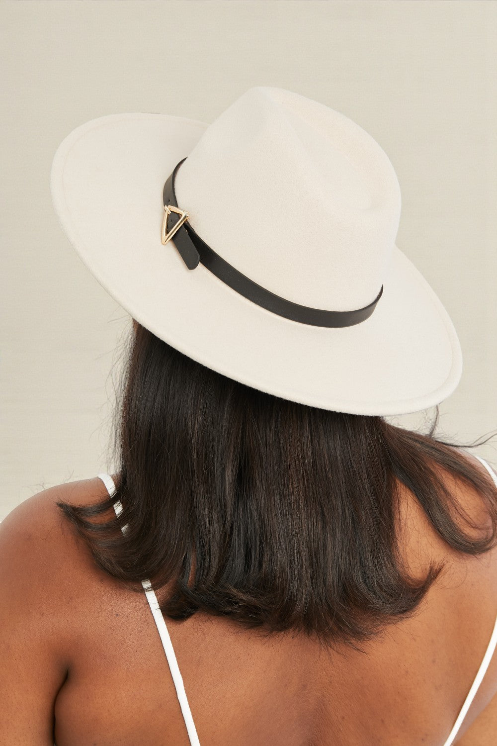 White fedora hat with a black band worn by a person on a beige background