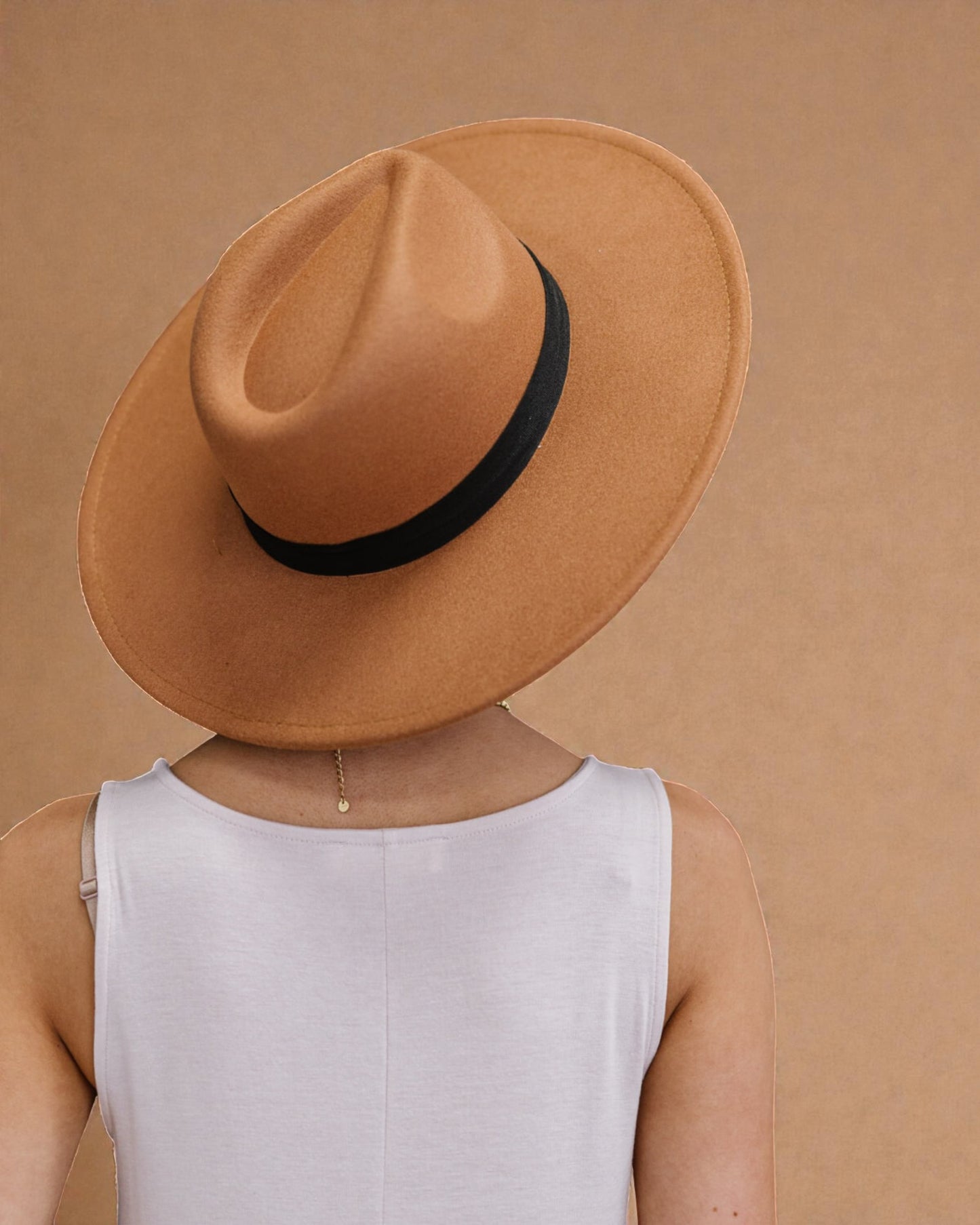 Person wearing a tan hat with a black band on a beige background