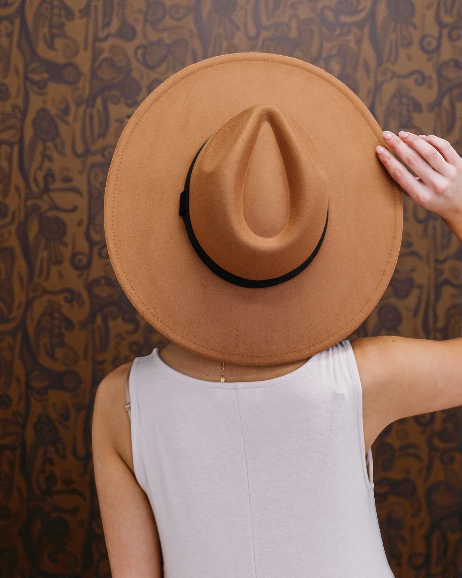 Person wearing a brown hat against a patterned wall