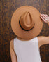 Person wearing a brown hat against a patterned wall
