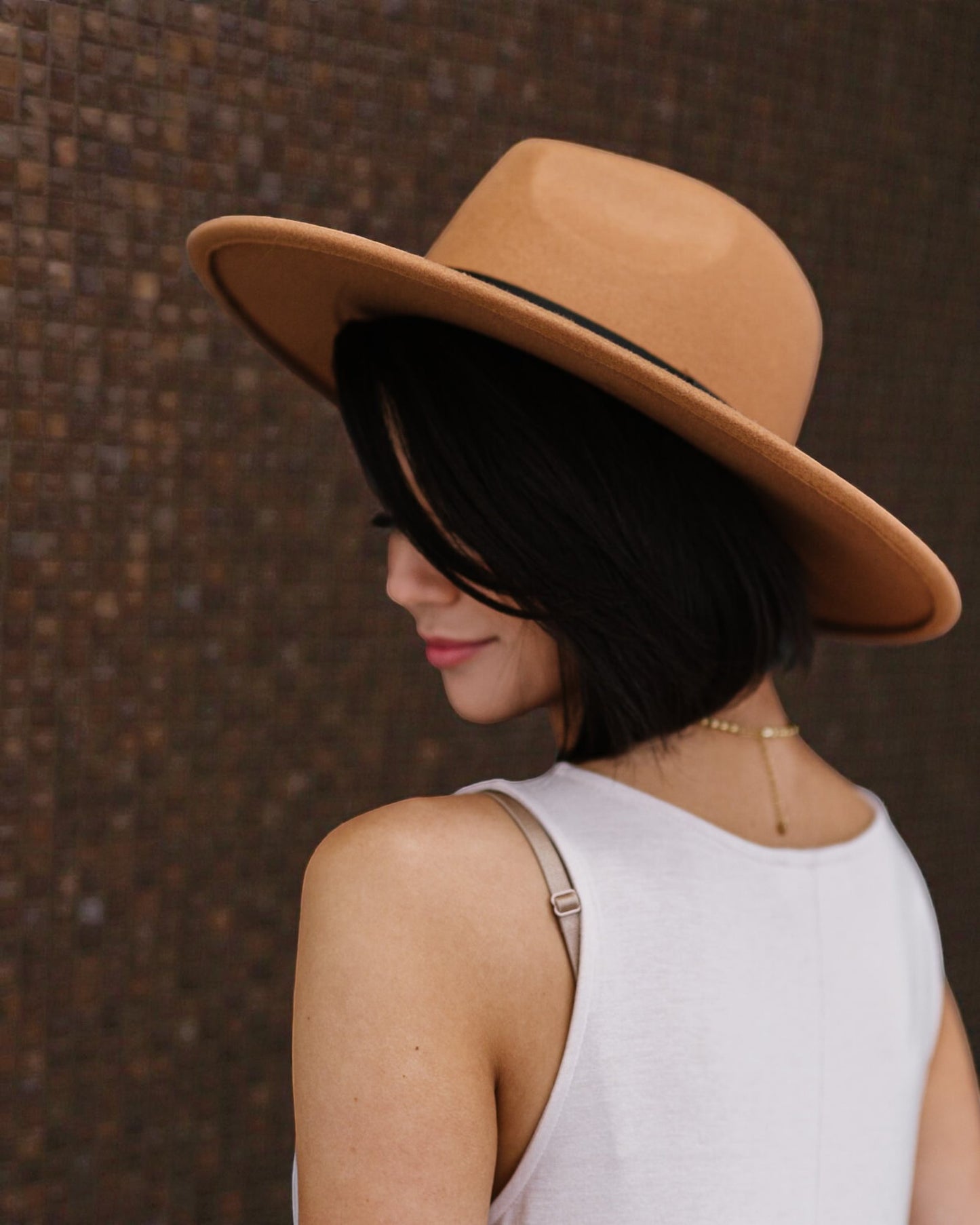 Woman wearing a wide-brimmed tan hat against a textured brown background