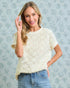 Woman wearing a textured white top and blue jeans against a light blue patterned background