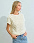 Woman wearing a textured cream top and blue jeans against a light gray background