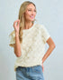 Woman wearing a textured cream top and jeans against a light blue background
