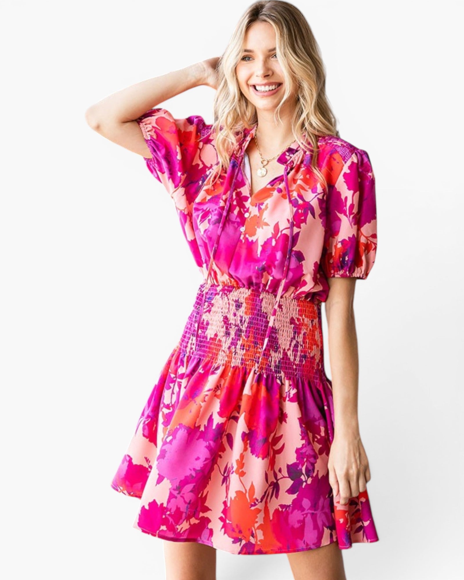 A woman modeling a short-sleeve mini dress with a vibrant pink, orange, and purple floral print against a plain white background.