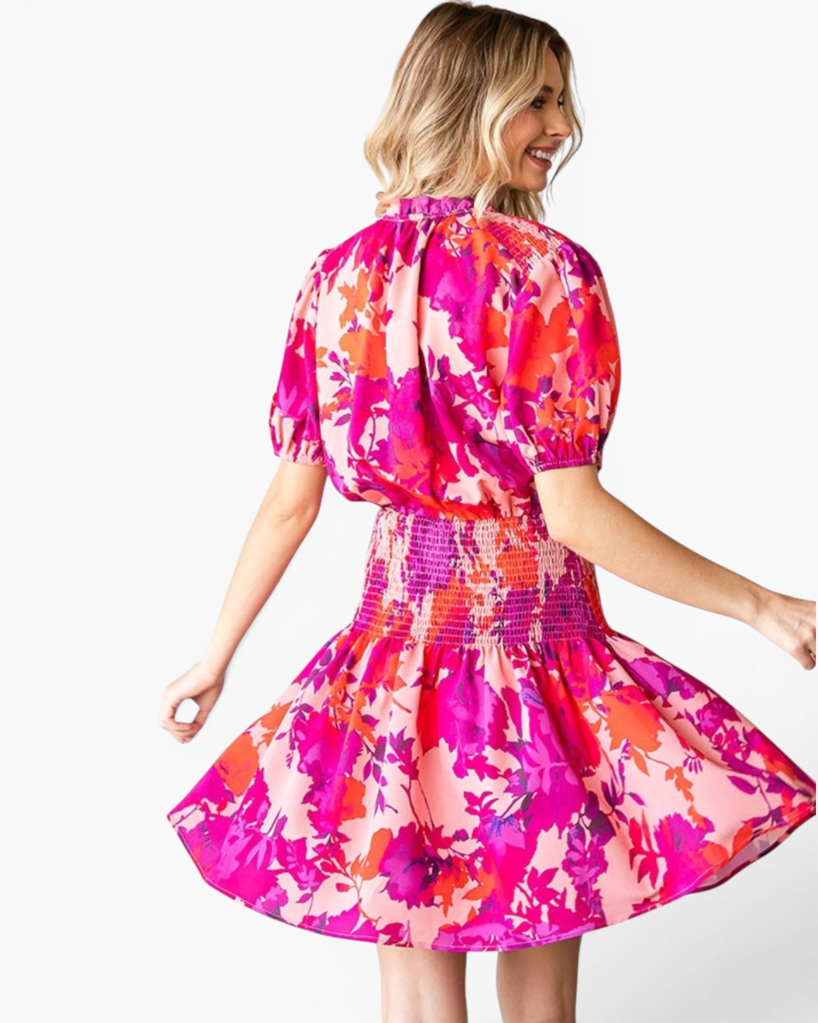 A woman wearing a short puff-sleeve dress with a vibrant pink, orange, and red floral print, shown from the back against a plain white background.