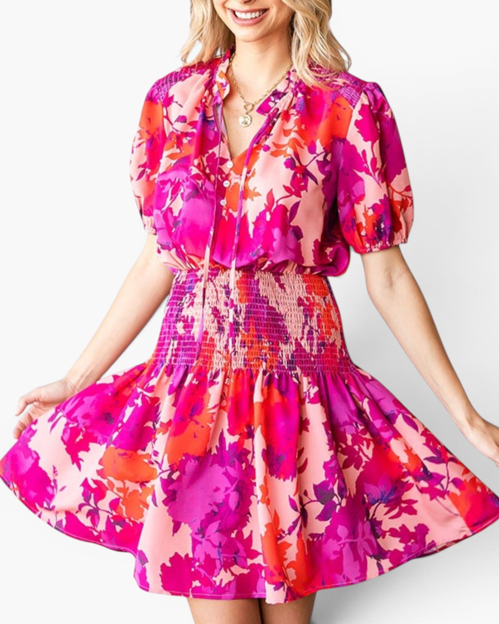 A woman wearing a short puff-sleeve dress with a vibrant floral print in hot pink, magenta, orange, and light pink, set against a plain white background.