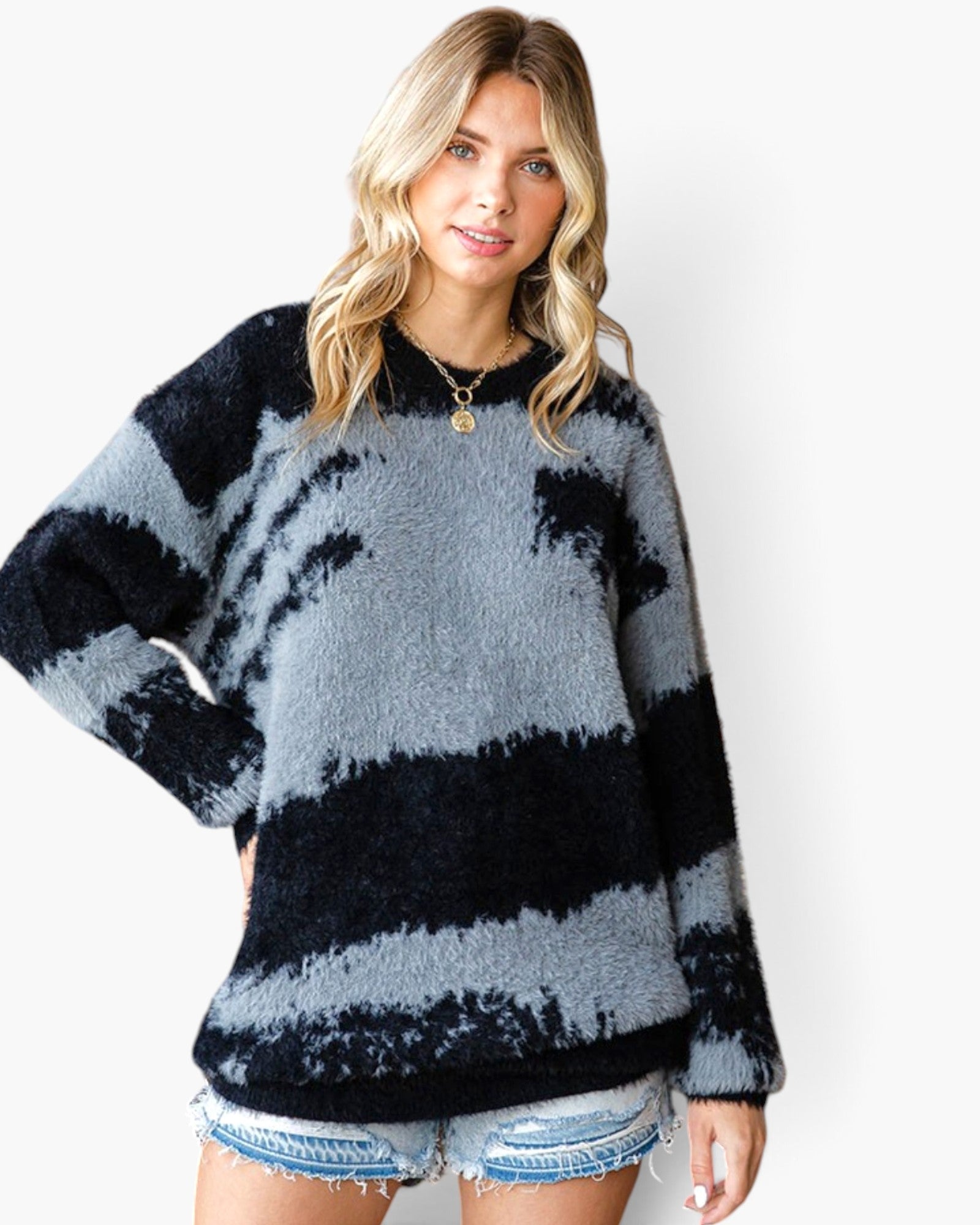 A woman wearing a fuzzy knit sweater with horizontal black and gray tie-dye stripes, paired with denim shorts, against a plain white background.