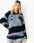 A woman wearing a fuzzy knit sweater with horizontal black and gray tie-dye stripes, paired with denim shorts, against a plain white background.